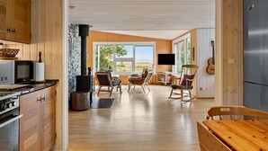 A spacious kitchen with wooden cabinets, a stove, and a microwave. There is a dining area with chairs and a table, and a large window offering a view of the outdoors.