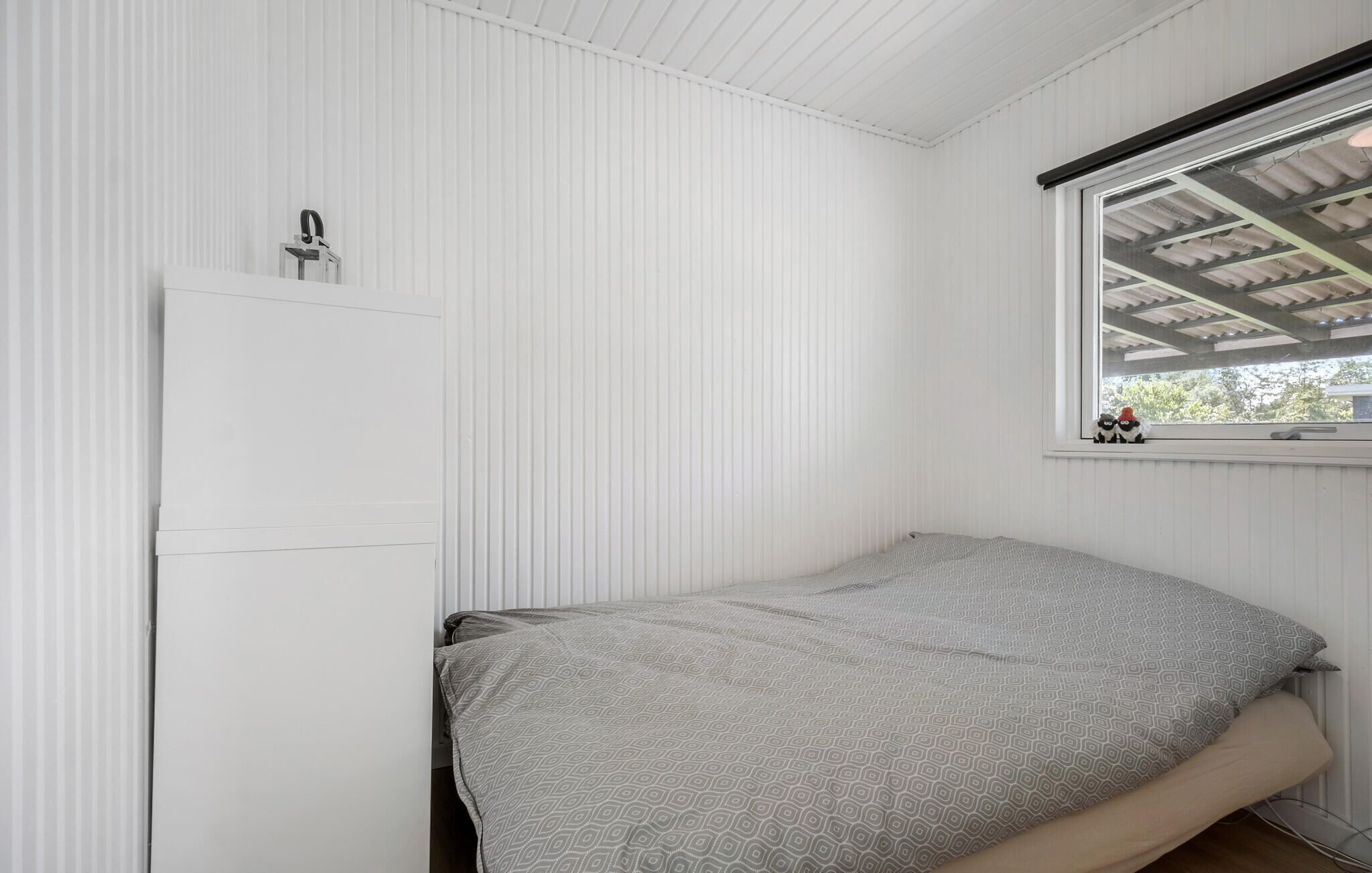 Une petite chambre avec un lit simple, une armoire blanche, une fenêtre donnant sur un paysage verdoyant et un plafond avec des poutres apparentes.