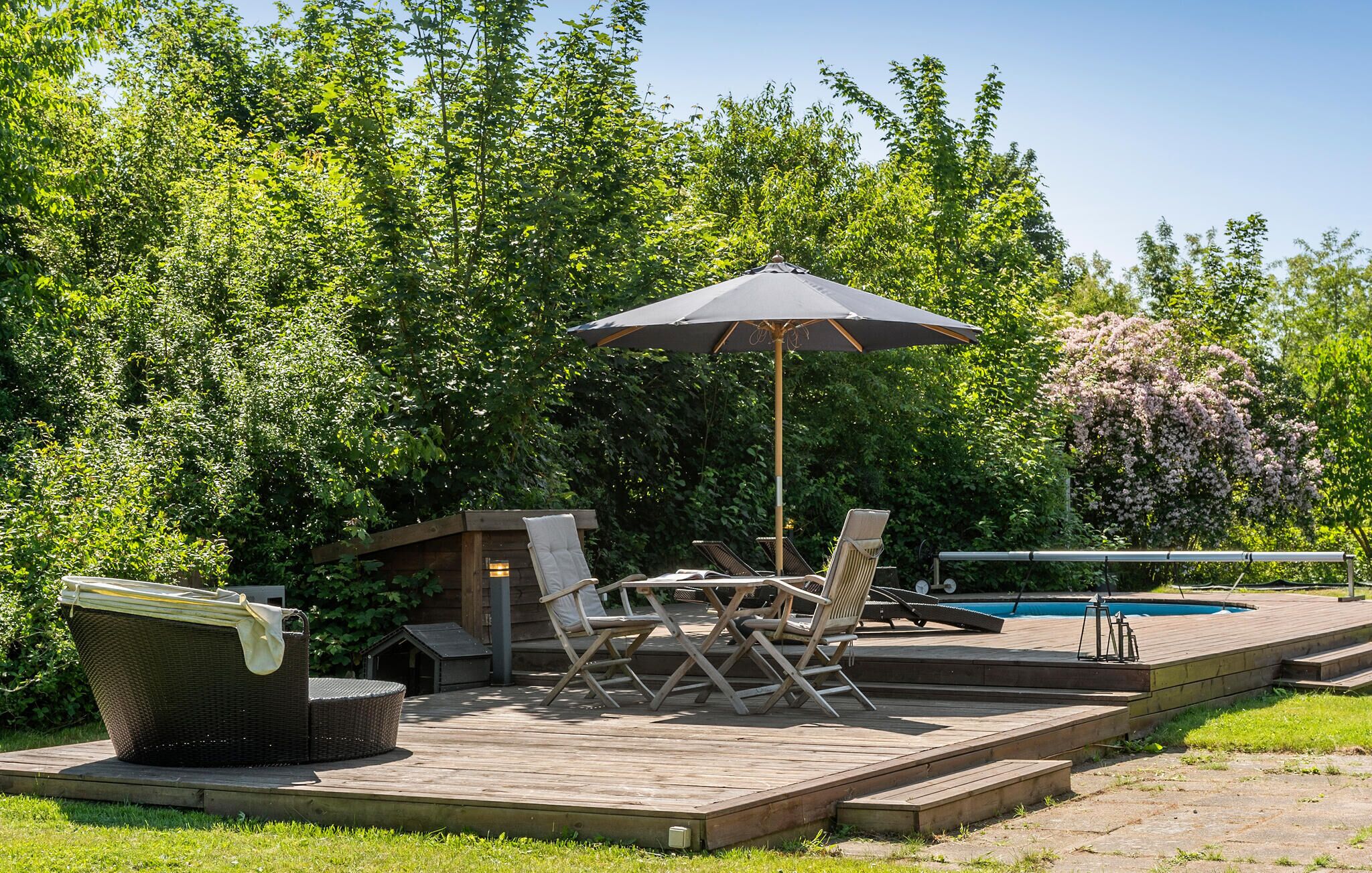 Une terrasse en bois avec des meubles d’extérieur, une piscine et une végétation luxuriante.