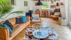 En hyggelig stue med en lædersofa, et glasbord og en kohude måtte. Reoler fyldt med bøger og et stort vindue giver naturligt lys.