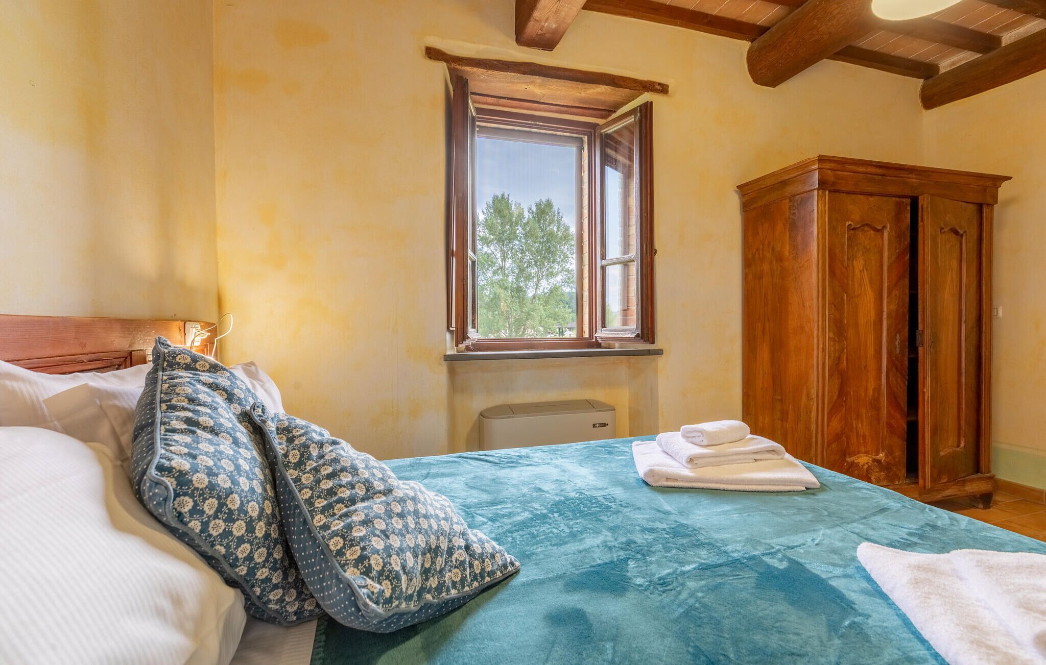 A bedroom with a bed, patterned pillows, a window, a wooden wardrobe, and a radiator.