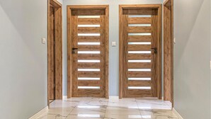 Un pasillo con dos puertas de madera con listones horizontales y suelo de mármol.