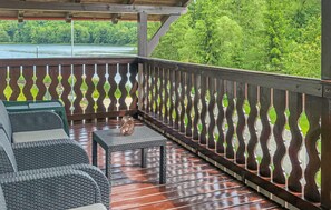 Un espace extérieur aménagé, abrité et doté de meubles en osier et d’une table, offrant une vue sur une étendue d’eau et une végétation luxuriante.