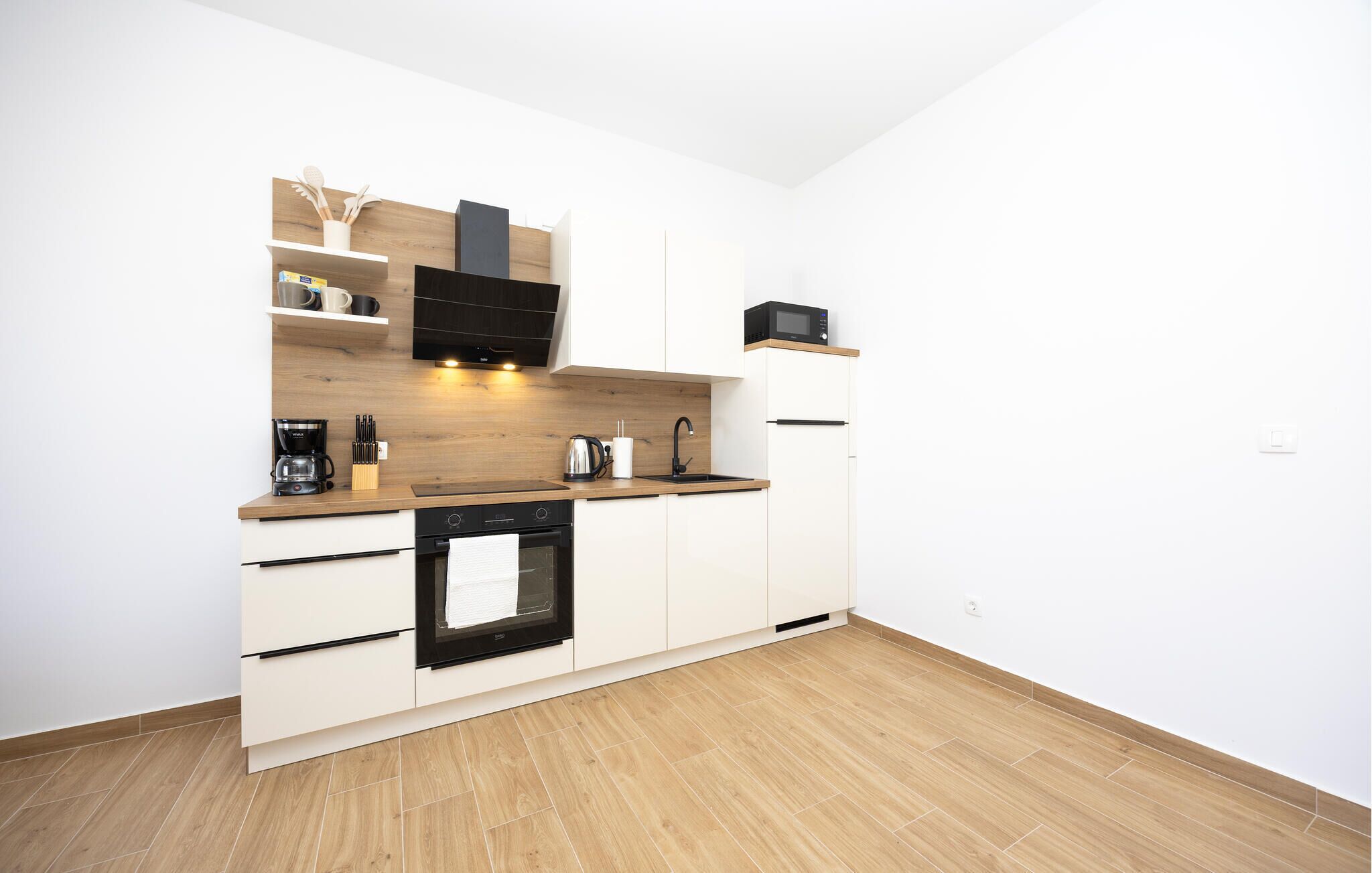 Een moderne keuken met witte kasten, een zwarte oven, een magnetron en een houten aanrecht.