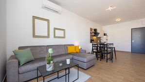 A modern living room with a grey sofa, a coffee table, and a dining area with a table and chairs. There is a kitchen in the background with cabinets and a countertop. - Lovely apartment in Seget Donji with WiFi (Seget Donji)