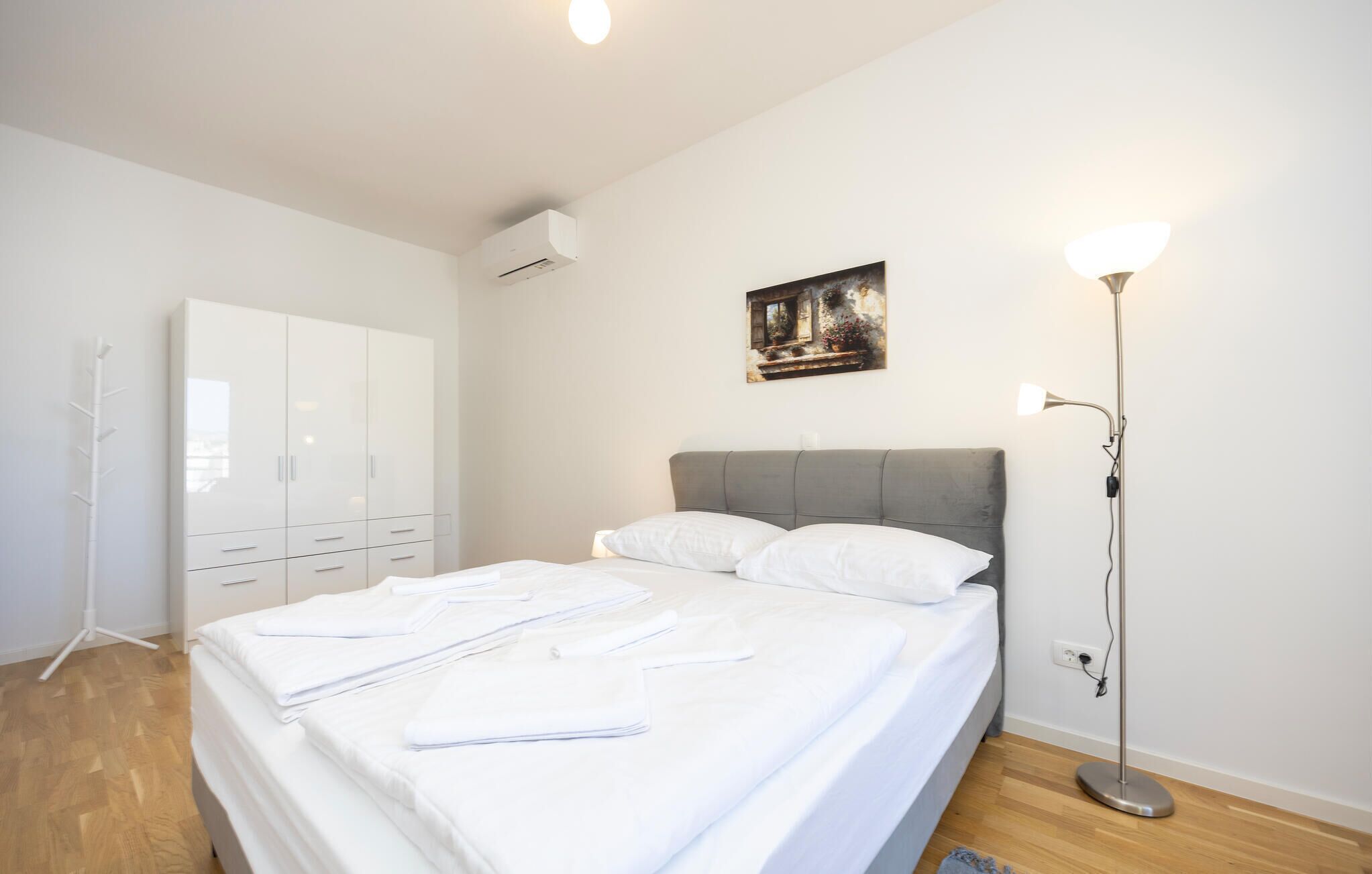 A bedroom with a bed, white wardrobe, and a painting on the wall.