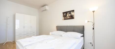 A bedroom with a bed, white wardrobe, and a painting on the wall.