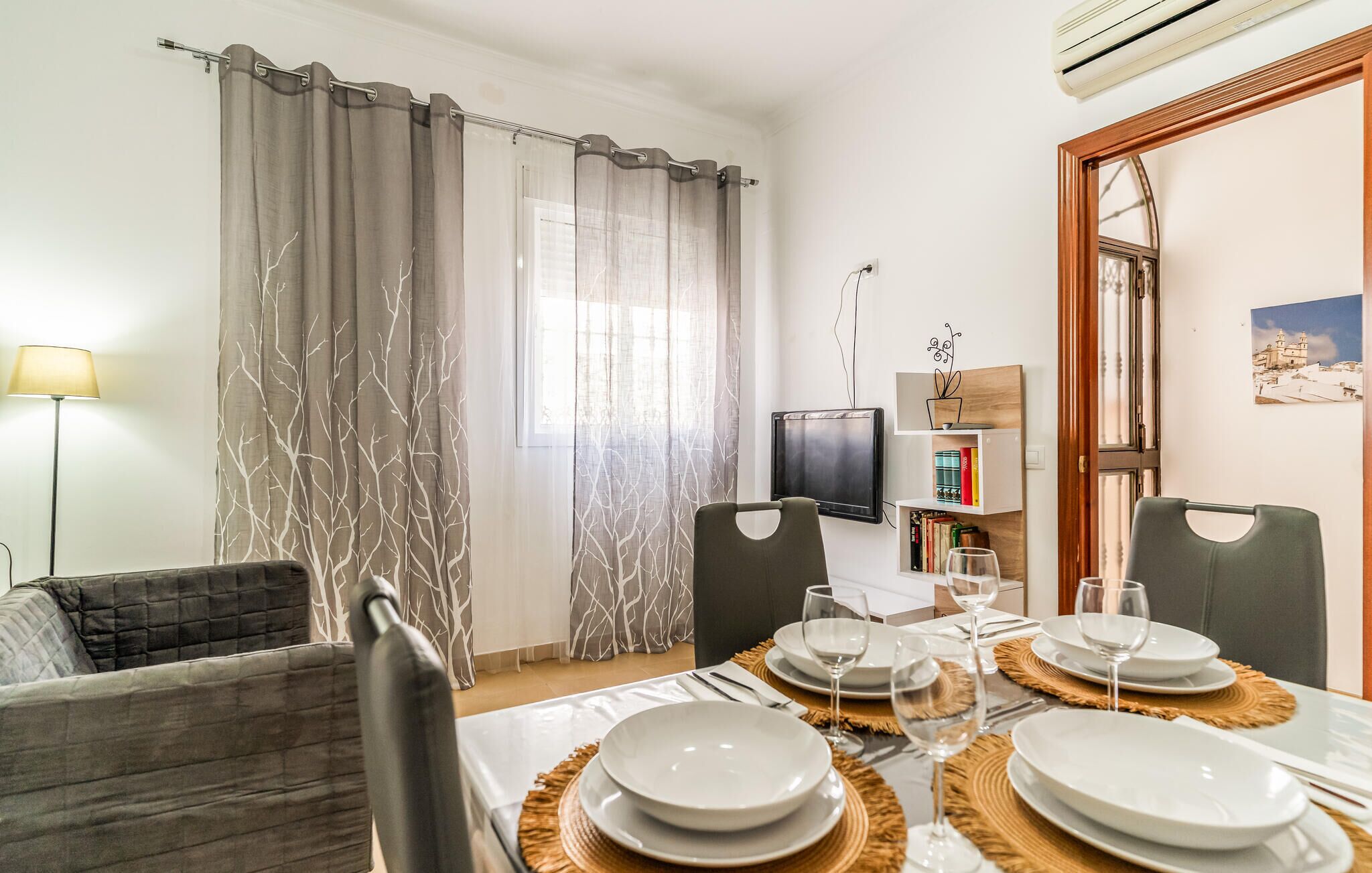 Zona pranzo con tavolo imbandito per quattro persone, divano, televisore e libreria.