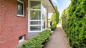 Une maison en briques rouges, avec une fenêtre à cadre blanc et un chemin de briques menant à un portail en bois.