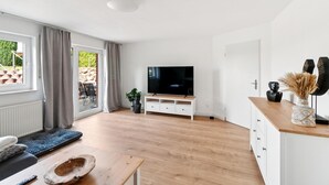 Un salon moderne doté d’un téléviseur à écran plat, d’un plancher en bois, d’un canapé, d’une table basse et d’une porte-fenêtre coulissante donnant sur un espace extérieur.