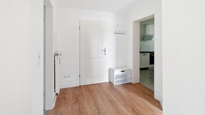 Un couloir étroit avec un plancher en bois, des murs blancs et une porte fermée.