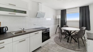 Une cuisine moderne avec des meubles blancs, un four encastré et un coin repas comprenant une table ronde et des chaises.