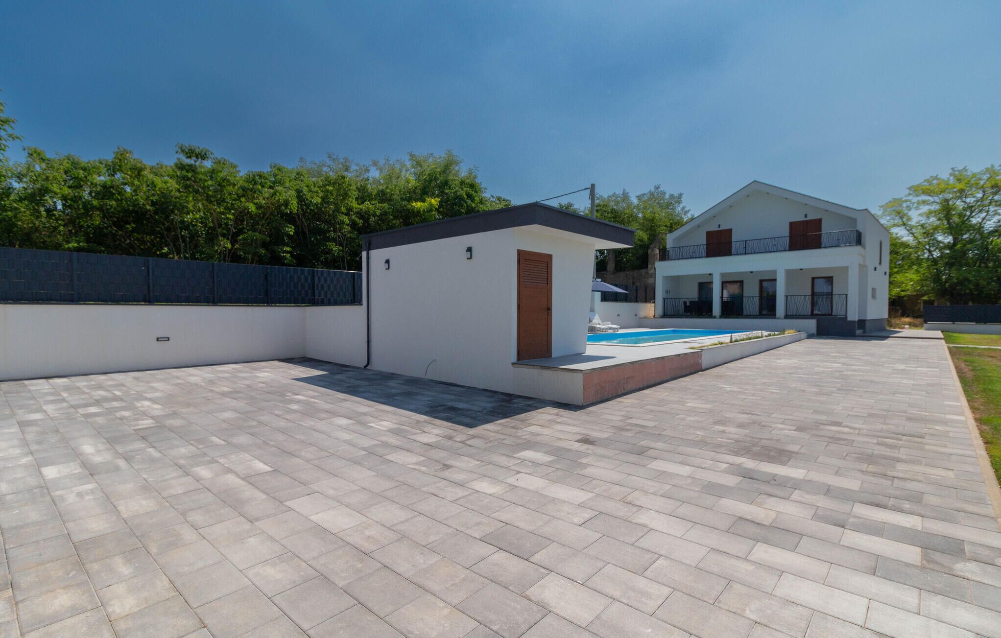 Una casa moderna con piscina, un pequeño garaje adosado y un patio empedrado.