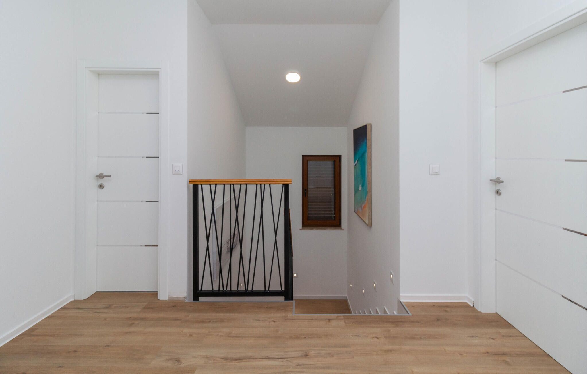 A hallway with wooden flooring, white walls, and a ceiling light. There are two doors on either side and a small table with a black metal frame.