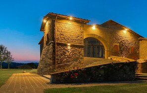 Un bâtiment en pierre avec un escalier menant à une porte, entouré d’une pelouse bien entretenue et sous un ciel dégagé.