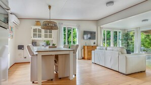 Ampla sala de estar com mesa de jantar, sofá e grandes janelas com vista para o verde.