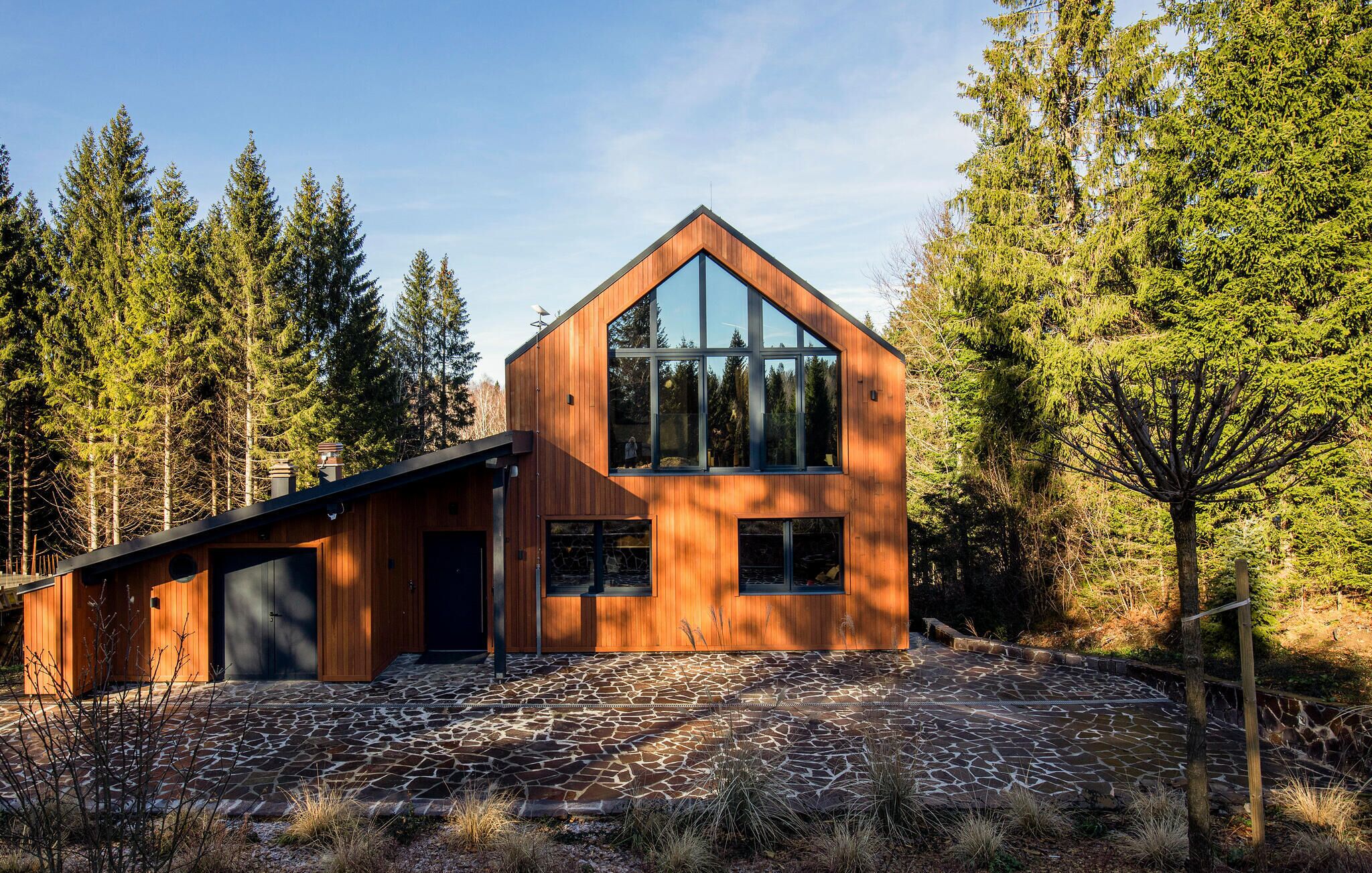 A modern wooden cabin with a sloped roof, large windows, and a stone-paved entrance.