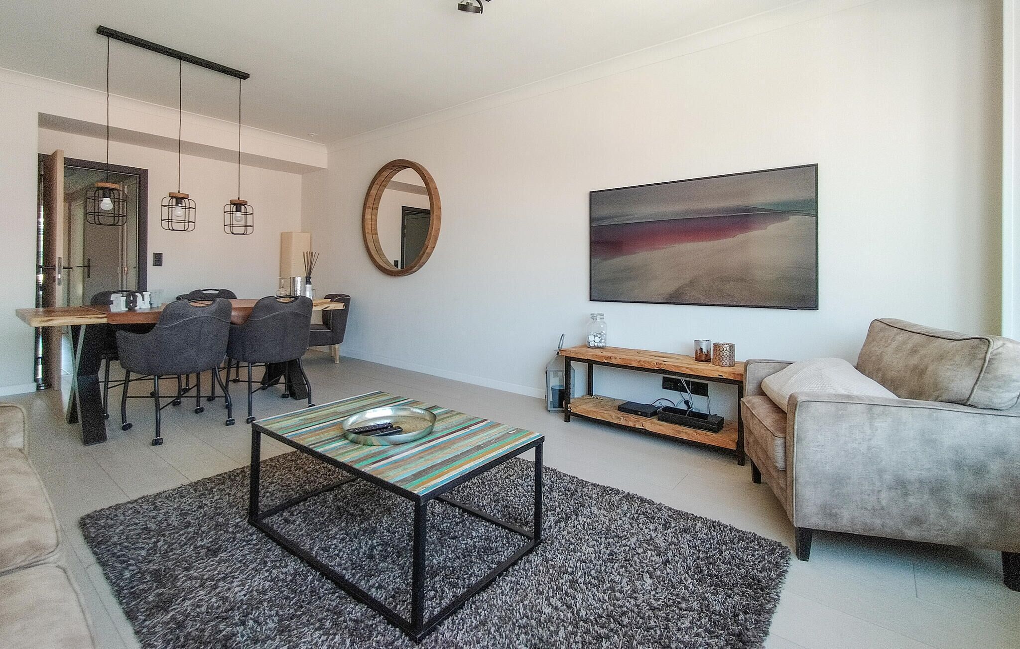 Een moderne woonkamer met een eethoek, een bank, een salontafel en een schilderij aan de muur.