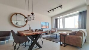 A modern living room with a dining area, featuring a round mirror, a wooden dining table, and a sofa. - Pet friendly apartment in Oostende with WiFi (Oostende)