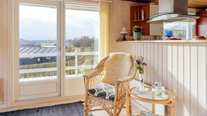 Et hyggeligt værelse med en fletstol, et rundt bord og udsigt til et boligområde gennem en skydedør.