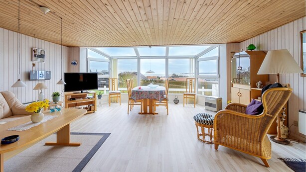 En rummelig opholdsstue med træloft, fjernsyn, spisebord og fletmøbler.