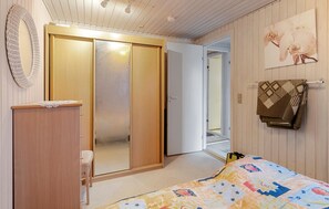 Un dormitorio con un armario de madera, una cama con colcha de colores, un escritorio pequeño y un perchero en la pared.