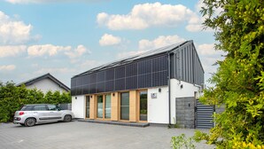 Una casa moderna con paneles solares, un automóvil estacionado en la entrada y un letrero con el número 5 en la pared.