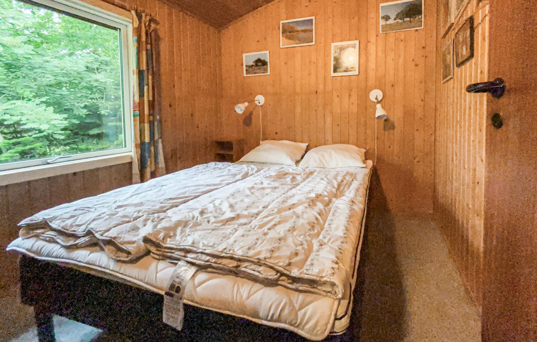 Et trægulvsrum med en seng, et vindue og vægmonterede lamper.