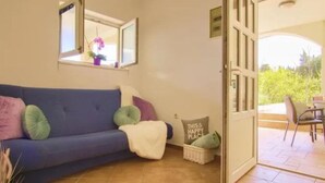 A room with a blue sofa, a window with a view, a door leading outside, and a small table with a chair. - Gorgeous apartment in Lukoran with WiFi (Lukoran)