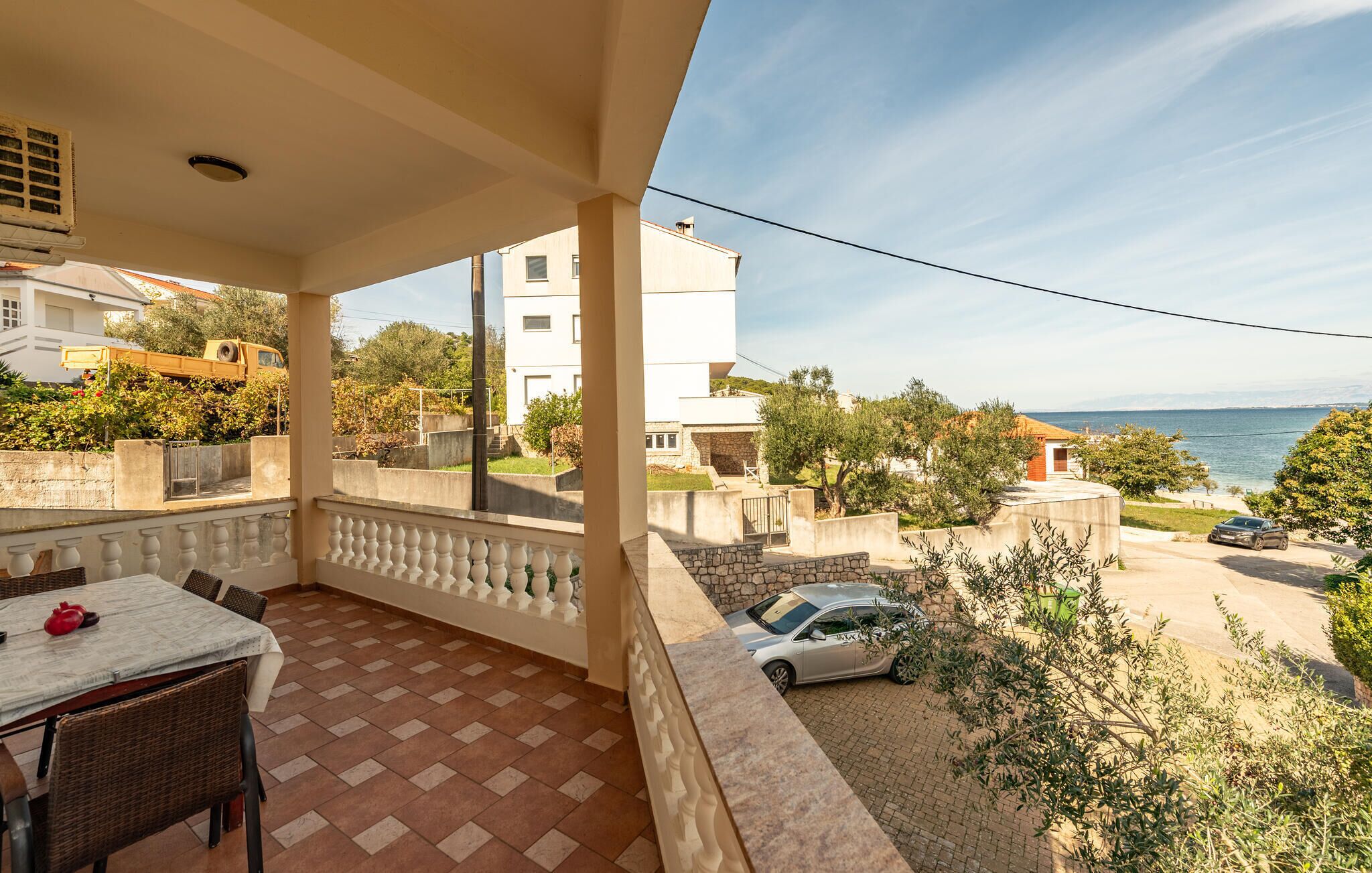 Un balcón con suelo de baldosas, una mesa con sillas y vistas al mar y edificios cercanos.