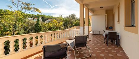 A balcony with two chairs, a table, and a view of greenery and houses.