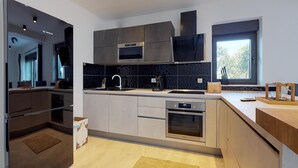 A modern kitchen with grey cabinets, a built-in oven, and a window with a view of trees. - Awesome apartment in Drenje (Drenje)