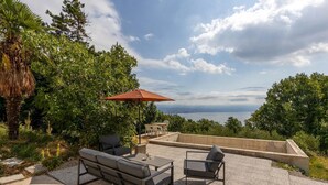 Un espace extérieur aménagé avec une table et des chaises, un parasol rouge et une vue sur la mer.