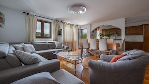 A modern living room with a sofa, armchairs, and a dining area with a table and chairs.
