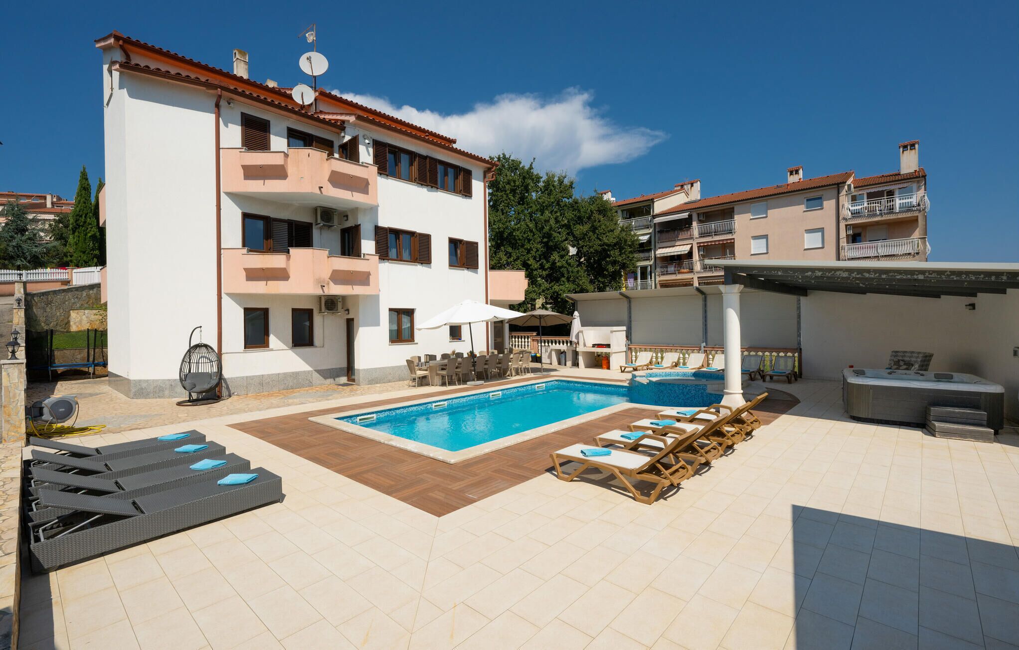 A two-story building with a swimming pool, outdoor seating, and a covered area with a grill.