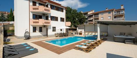 A two-story building with a swimming pool, outdoor seating, and a covered area with a grill.
