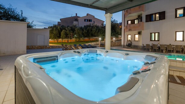 A hot tub with a tiled floor, a covered patio area, and a building in the background.