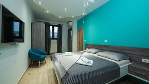 A modern bedroom with a large bed, a TV mounted on the wall, a chair, and a view of the outdoors through the window.