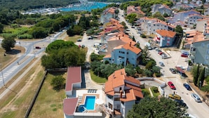 A residential area with a swimming pool, multiple-story buildings, and a marina in the background.