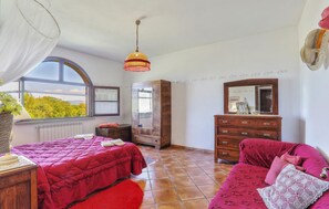 Een slaapkamer met een groot raam, een houten dressoir, een spiegel en een rode bank.