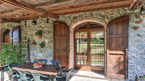 Un bâtiment rustique en pierre, doté de portes en bois et d’un patio couvert avec une table et des chaises.
