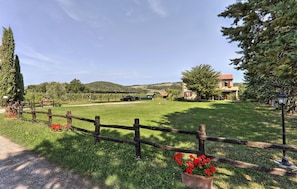 A rural landscape with a wooden fence, a building with a red roof, and a clear sky.