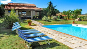 Un espace aménagé au bord de la piscine, avec des chaises longues, une piscine et une maison dotée d’un toit en tuiles.