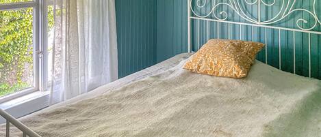 A bed with a patterned pillow, a metal headboard, and a window with curtains.