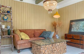 Un salon avec un canapé à motifs, une table basse en verre, un meuble en bois, un lustre et une étagère murale agrémentée d’objets décoratifs.
