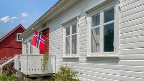 A white wooden house with a red door and windows, a flag, and a small porch. - 4 bedroom pet friendly home in Farsund (Farsund)