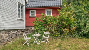 A red house with a stone wall foundation, a small table with two chairs, and a garden with green foliage. - 4 bedroom pet friendly home in Farsund (Farsund)