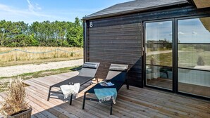 En modern uteplats med två solstolar och ett bord, med utsikt över en gräsklädd äng.