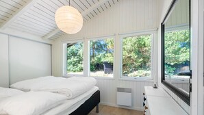 A bedroom with a bed, a radiator, and three windows offering a view of greenery.