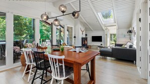 A spacious living area with a wooden dining table, white chairs, a sofa, and a fireplace.